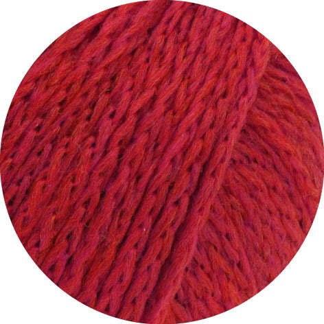 vrouw in een koraalrode trui naast een tafel als inspiratie voor Lana Grossa Cool Merino Big 231 Roze - Lana Grossa Cool Merino Big 201 Ruw Wit